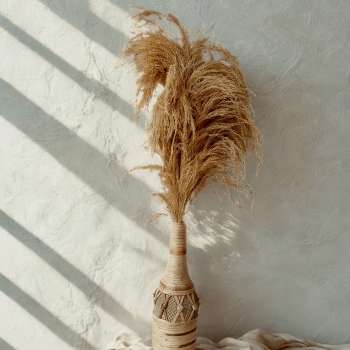 A bottle shaped flower vase wrapped in the finest selection of the raffia plats, with slight contrast in tones which ties it together. It is filled with pampas grass which is designed to last but as a filler