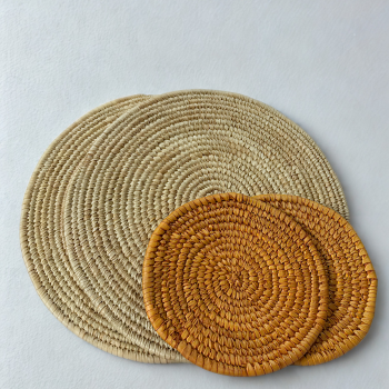 Beige woven placemats and orange trivets arranged on a natural surface in warm daylight. dinner sets in nigeria