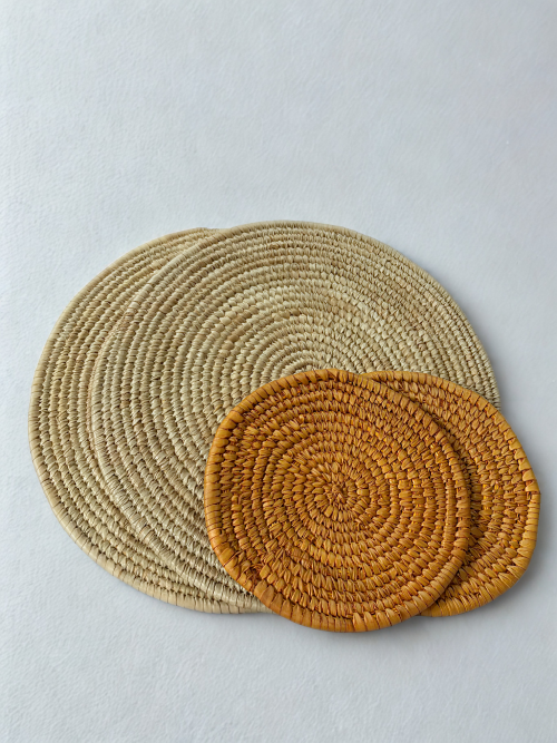 Beige woven placemats and orange trivets arranged on a natural surface in warm daylight. dinner sets in nigeria
