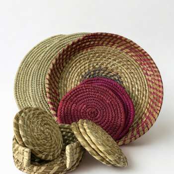 Beige placemats, purple trivets, and wave tray styled with woven coasters on dining table. Handcrafted table set in beige and purple tones with natural fiber texture. The Essence Set by Aduné featuring artisanal placemats, trivets, and coasters. Minimalist home decor set in warm neutral and purple hues.